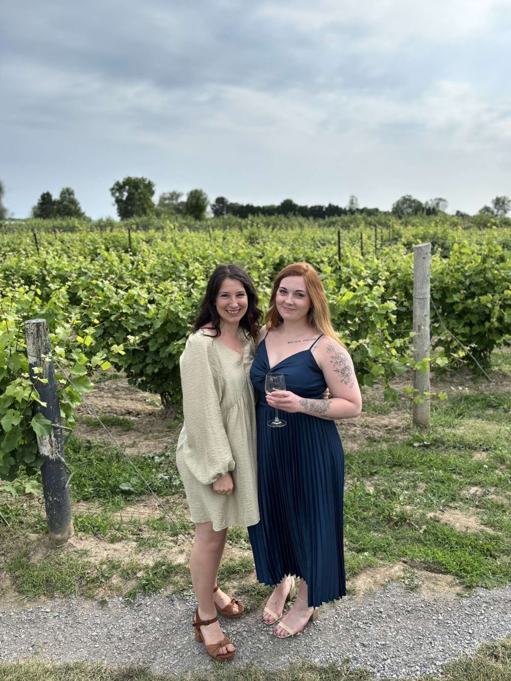 Two friends enjoying a sunny day together at a vineyard with rows of grapevines stretching into the distance.