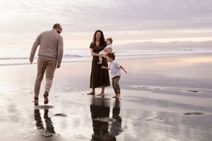 mum holding daughter and son chasing dad at the beach during sunrise session, Christchurch