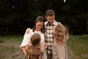 Mum and dad looking down at kids cuddling in during family session at Bottle lake forest Christchurch