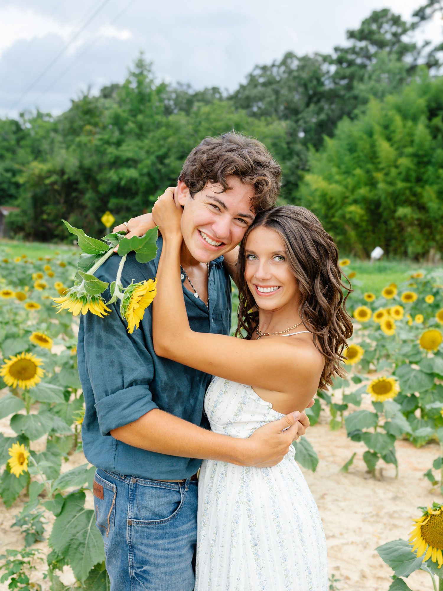 A couple embraces in a vibrant sunflower field during a summer photoshoot.