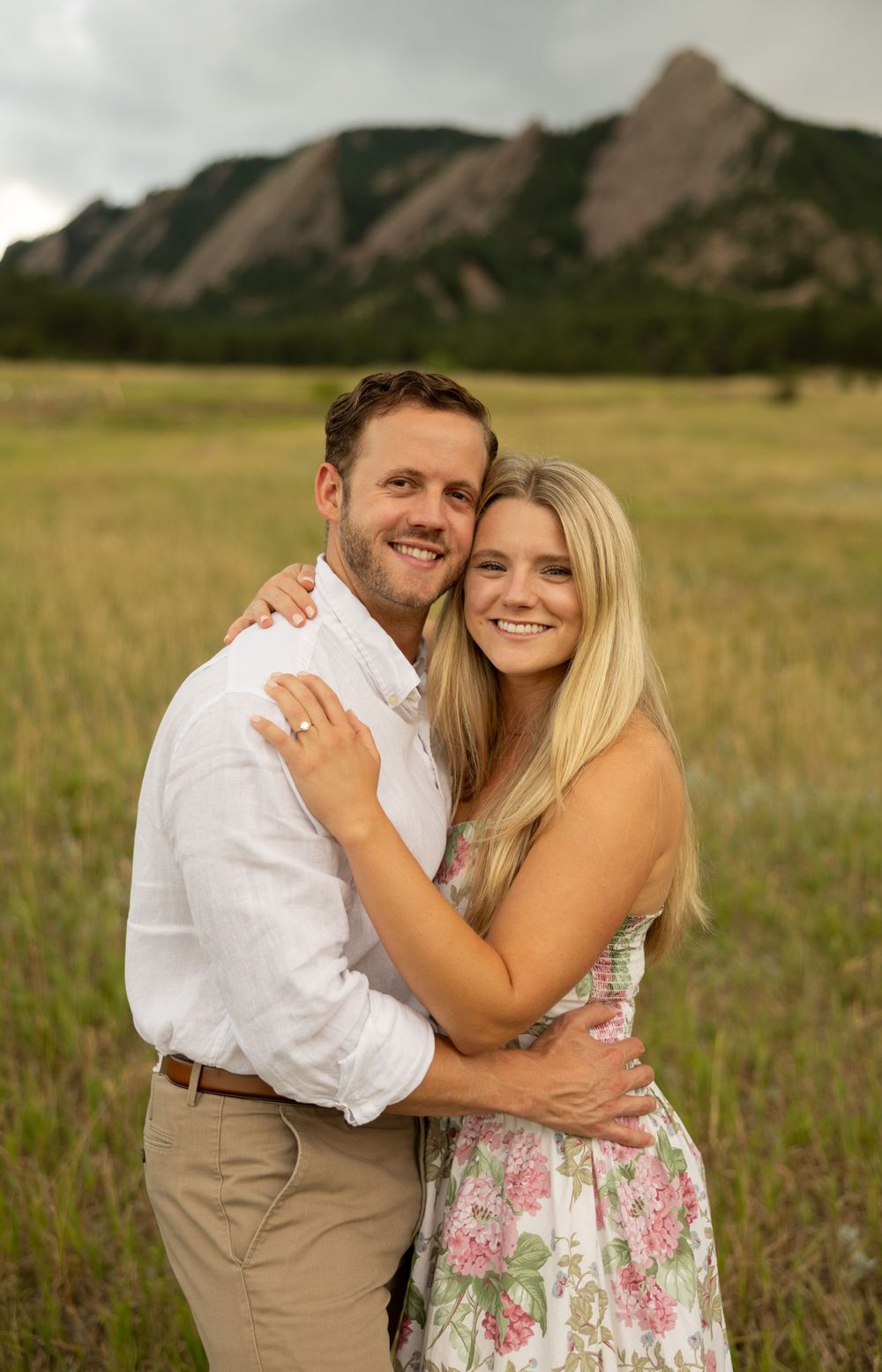 A joyful embrace in a Colorado meadow with the distinctive Flatirons rock formation visible behind.