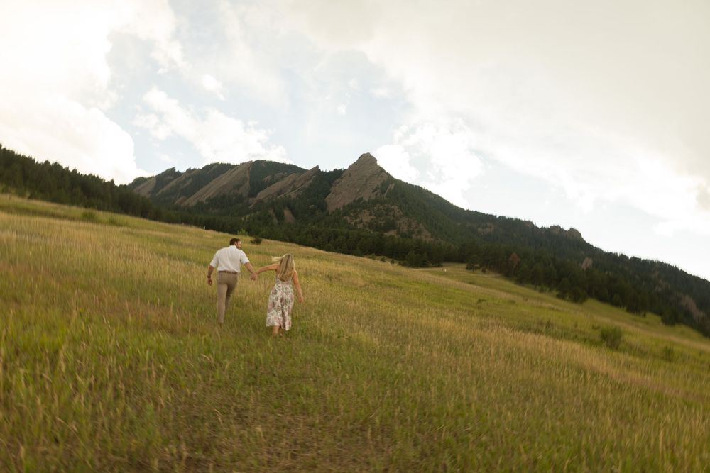 Two figures walk through a sunlit meadow towards the Flatirons mountains in Boulder.