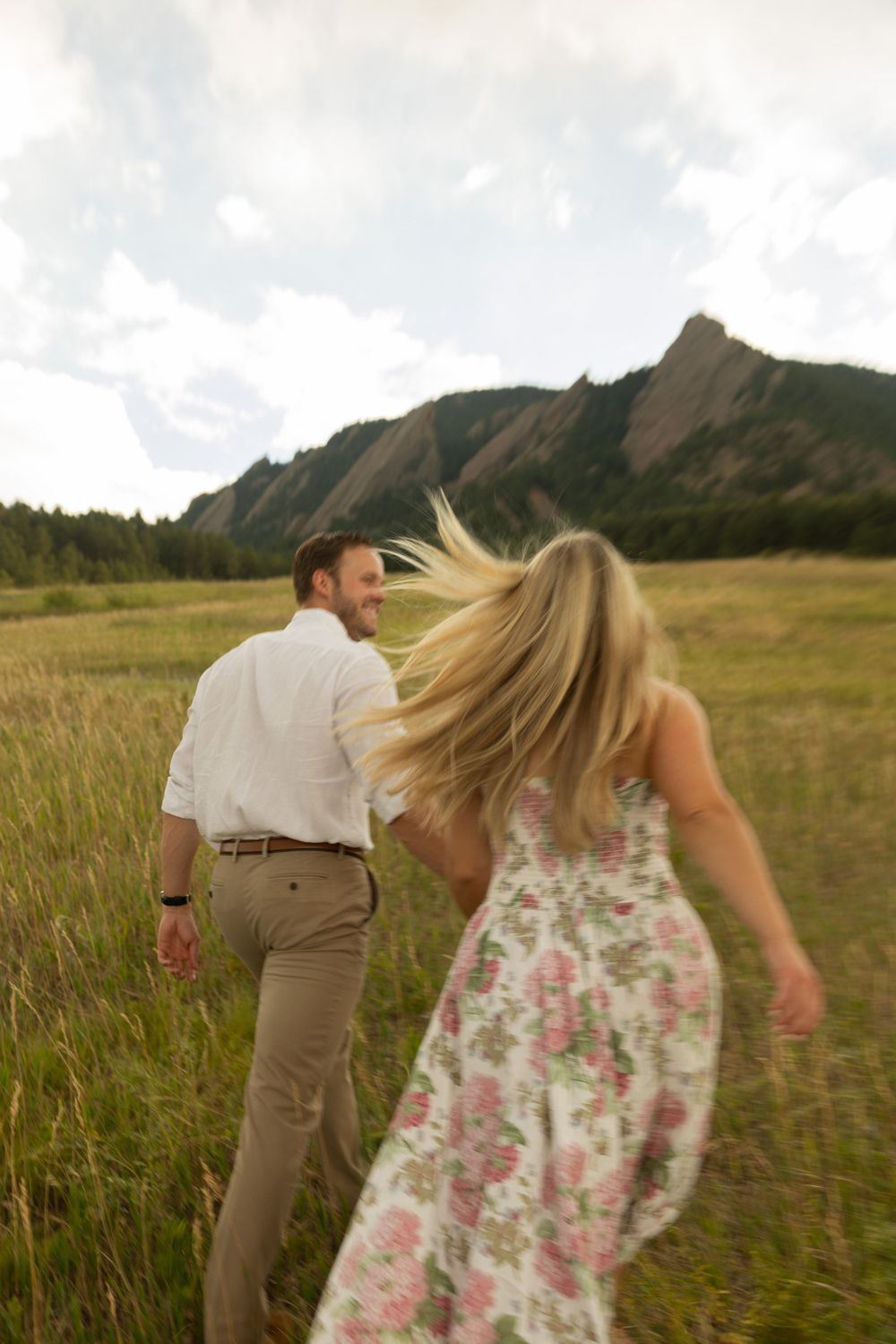 Couple walking through a golden meadow with the Flatirons mountains of Boulder Colorado in the background.