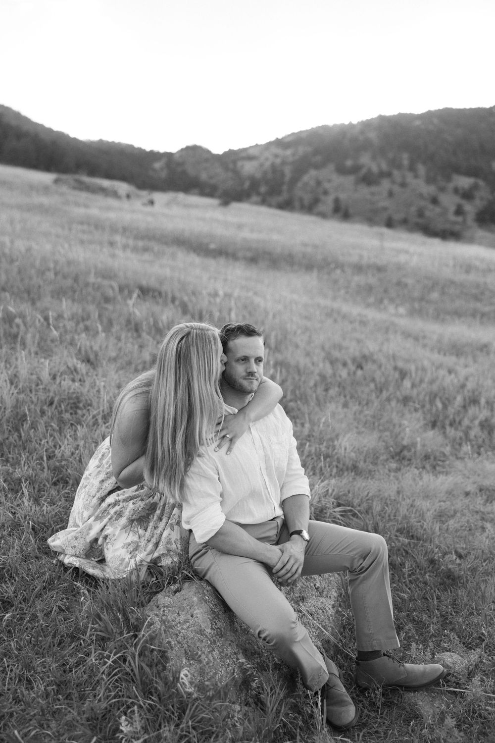 Black and white portrait of couple sitting on rock in mountain meadow.