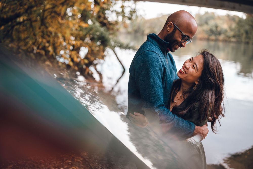 A romantic couple embraces by a serene lake during autumn with golden foliage in the background at Theodore Roosevelt Island in DC.