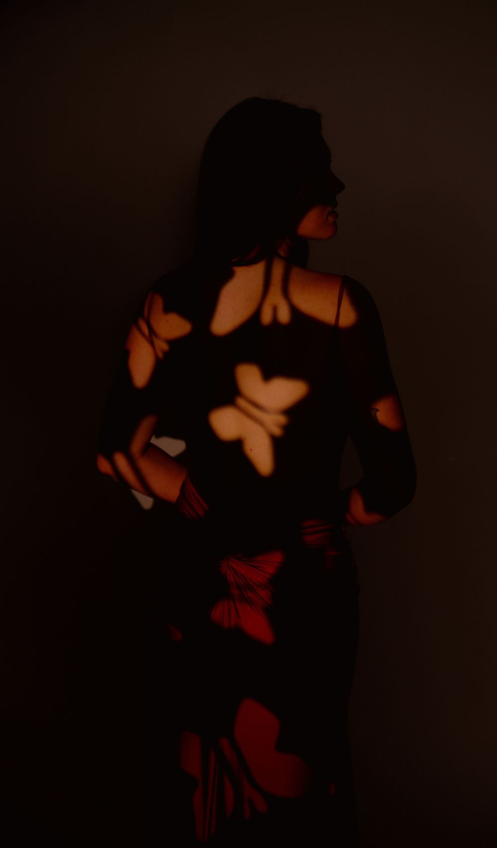 Silhouetted figures in dark moody lighting create dramatic shadows against a reddish-orange background.