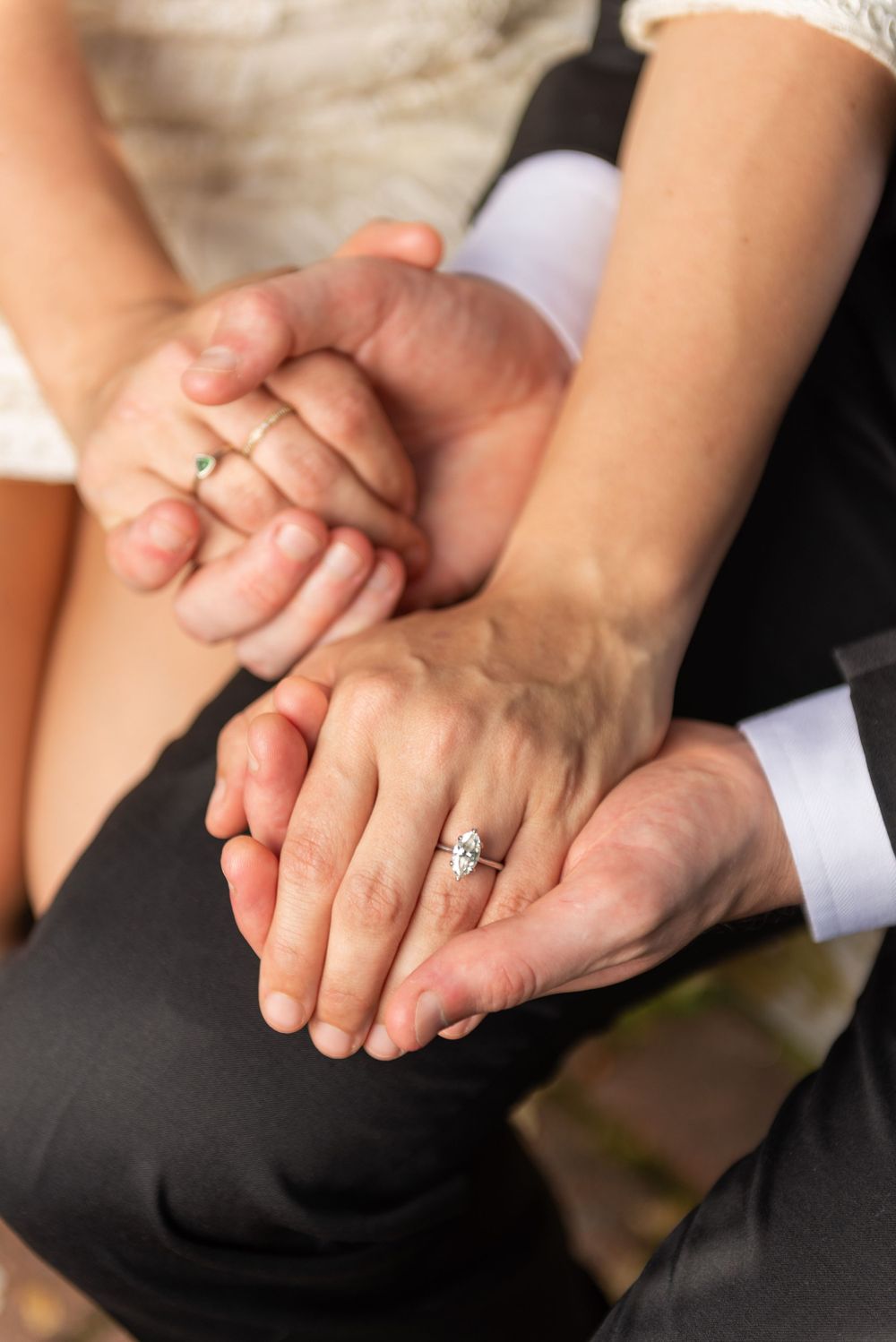 Close-up of hands with engagement rings showing a tender moment between a couple in formal wedding attire.