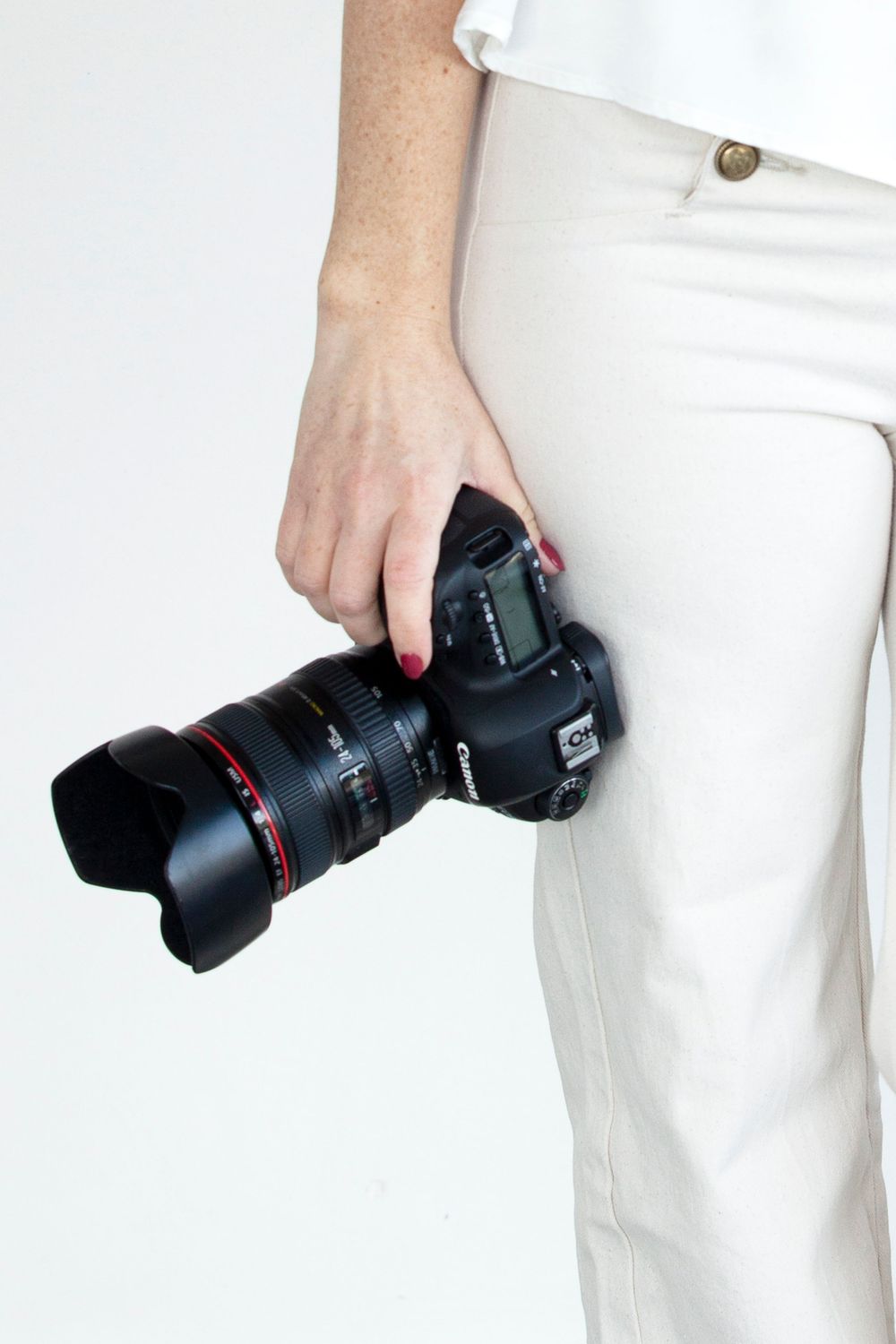 Main tenant un appareil photo reflex numérique professionnel avec téléobjectif sur fond de pantalon blanc.