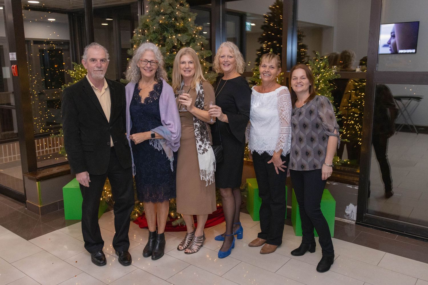 A group posing together at a holiday event with decorated trees in the background.