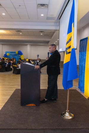 Speaker stands at podium with Ukrainian flag during formal event.