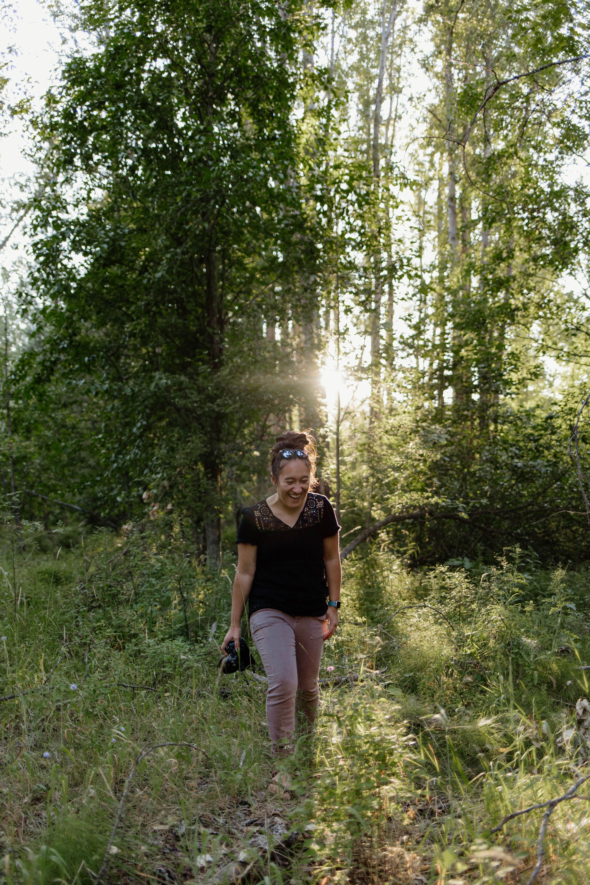 Sunlight streams through forest trees as a person walks along a nature trail on a summer evening.