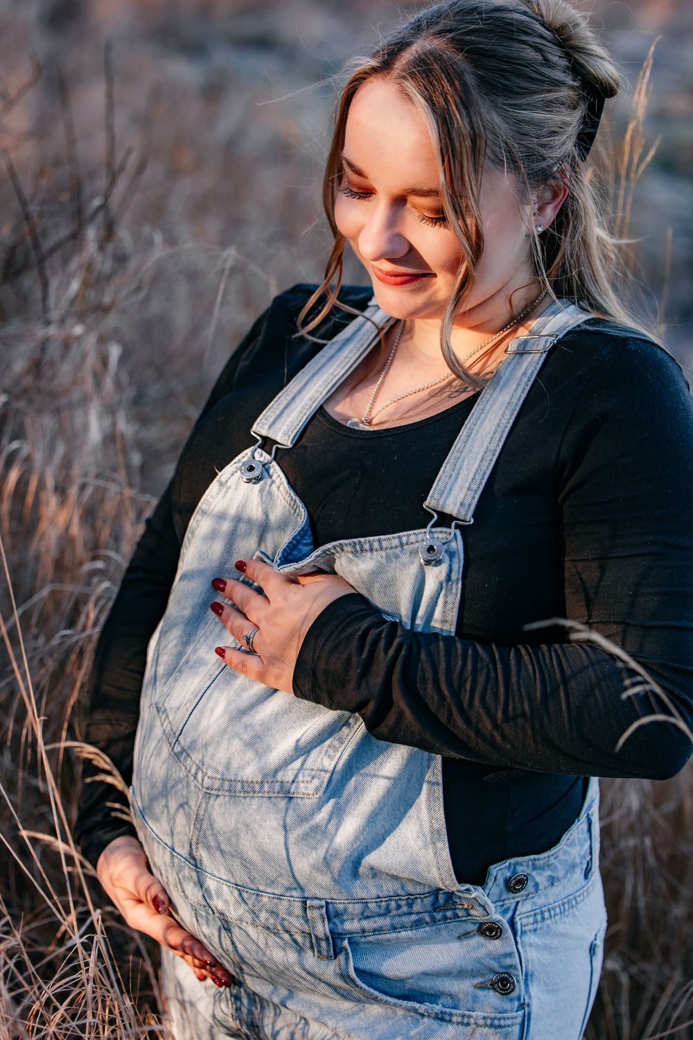 babybauchshooting winterliches wetter die werdende mama am Waldrand an einem Feld mit Gräsern