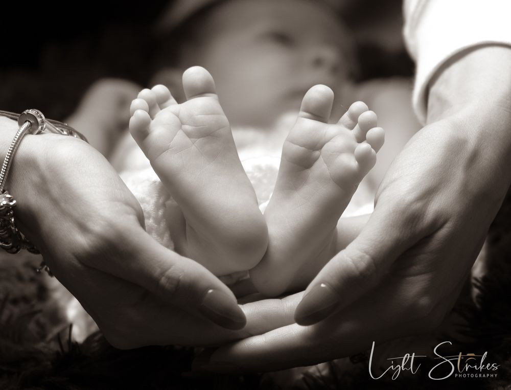 Newborn photographer captured artistic image in black and white close-up of tiny baby feet in adult hands showing tender family moment.