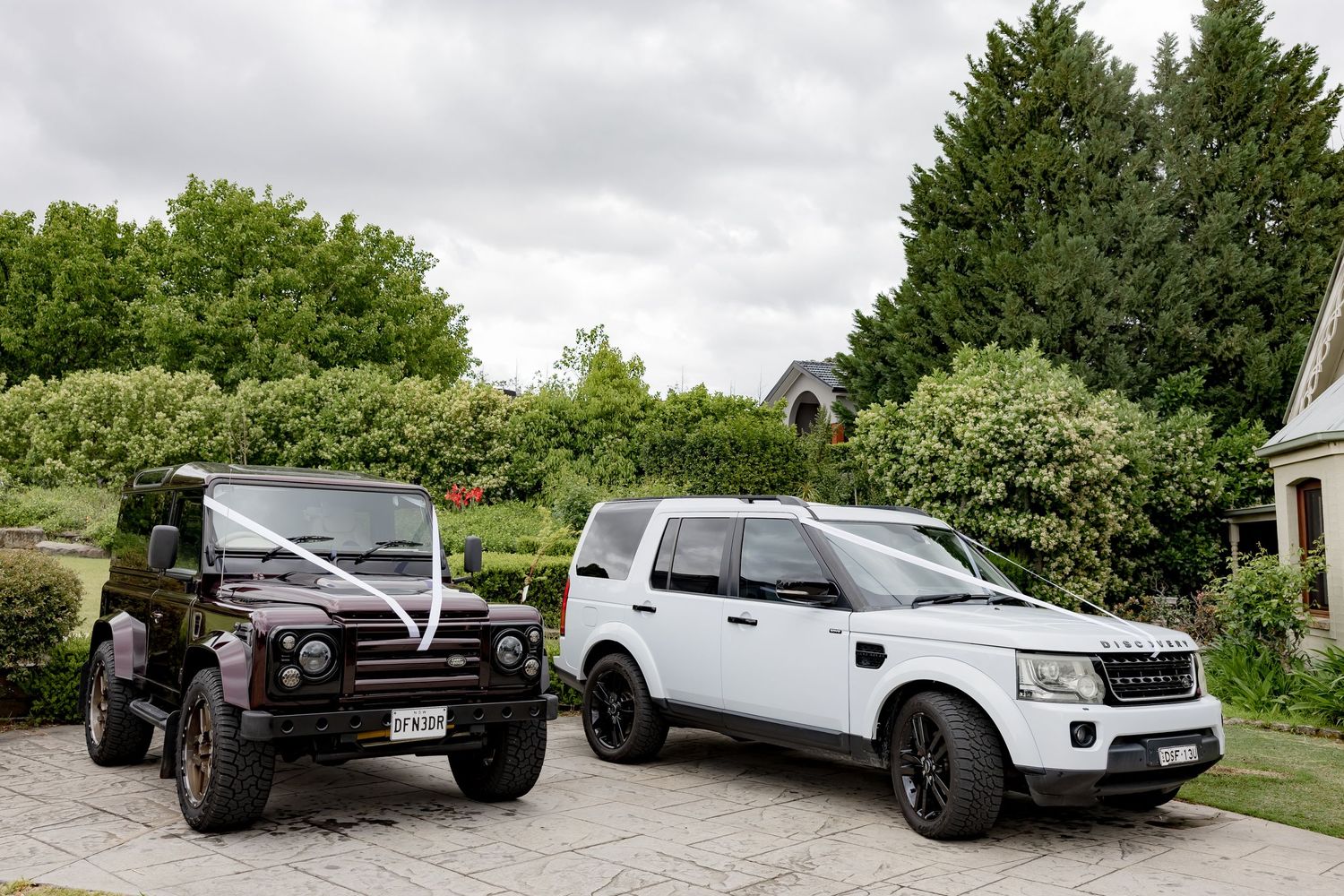 Two luxury SUVs parked in a driveway, a black Land Rover Defender and white Land Rover Discovery.