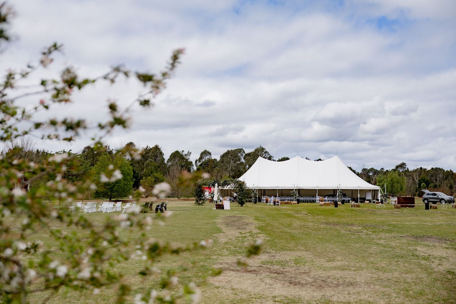 Large white wedding tent set up in an open field with trees in background.