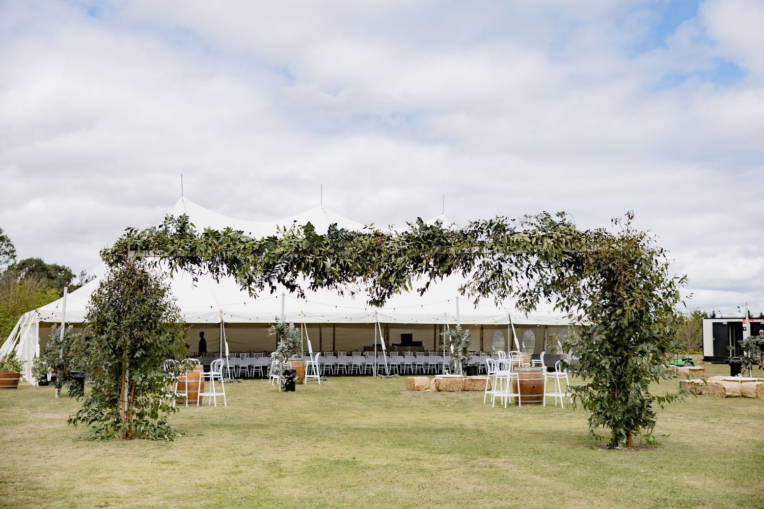 Large white wedding tent with floral archways and string lights set up on a grassy field.