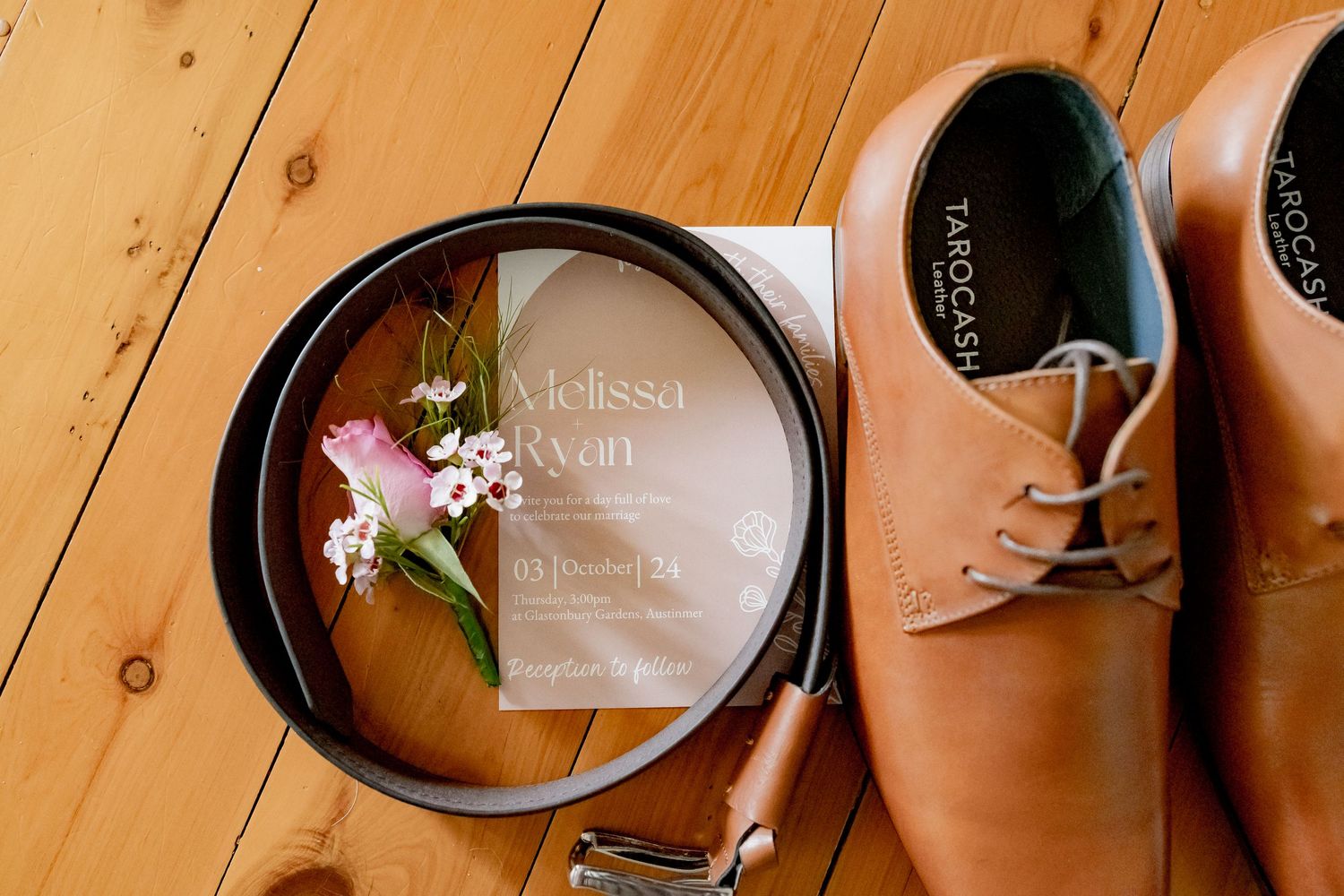 Wedding invitation and groom's accessories artfully arranged on wooden surface.