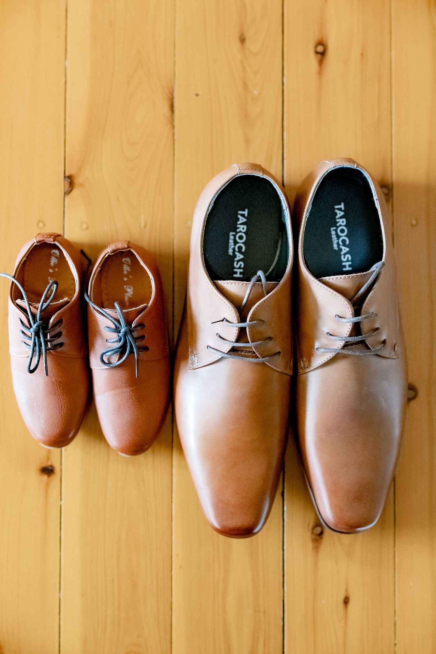Two pairs of tan leather dress shoes arranged on wooden flooring.