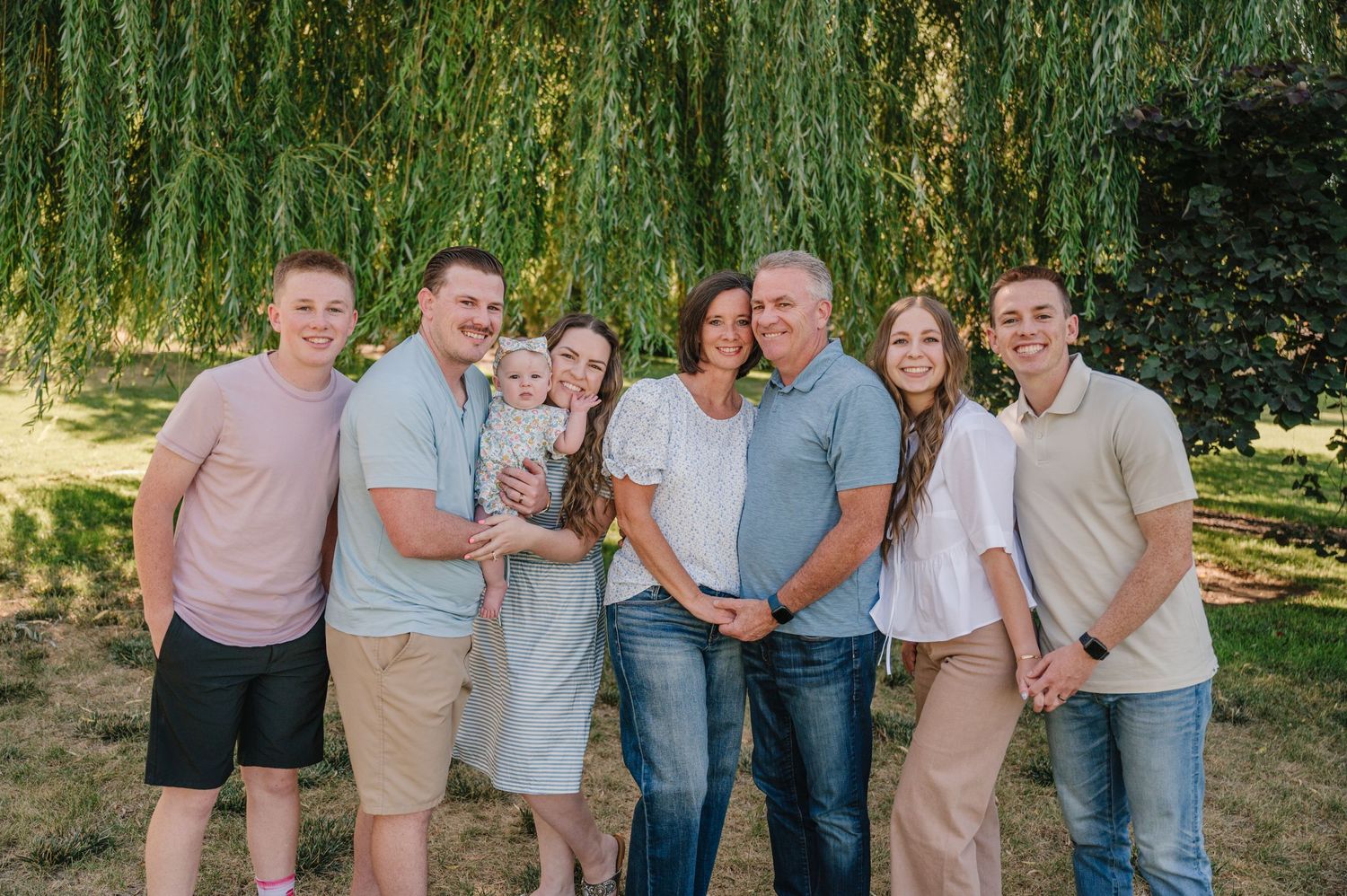 Family gathering under a weeping willow tree on a sunny summer day.