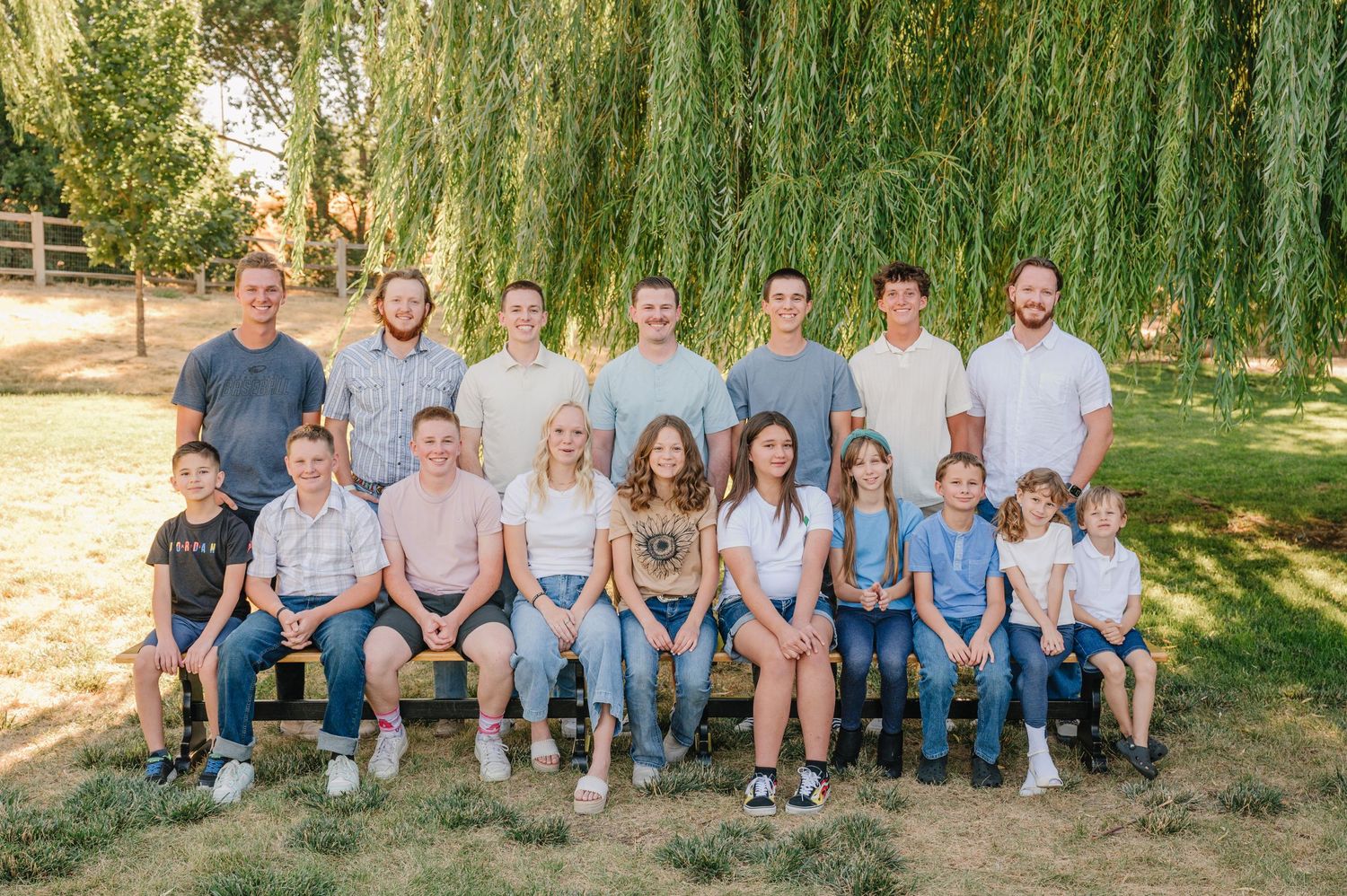 Large group portrait of extended family members seated in rows under willow trees.