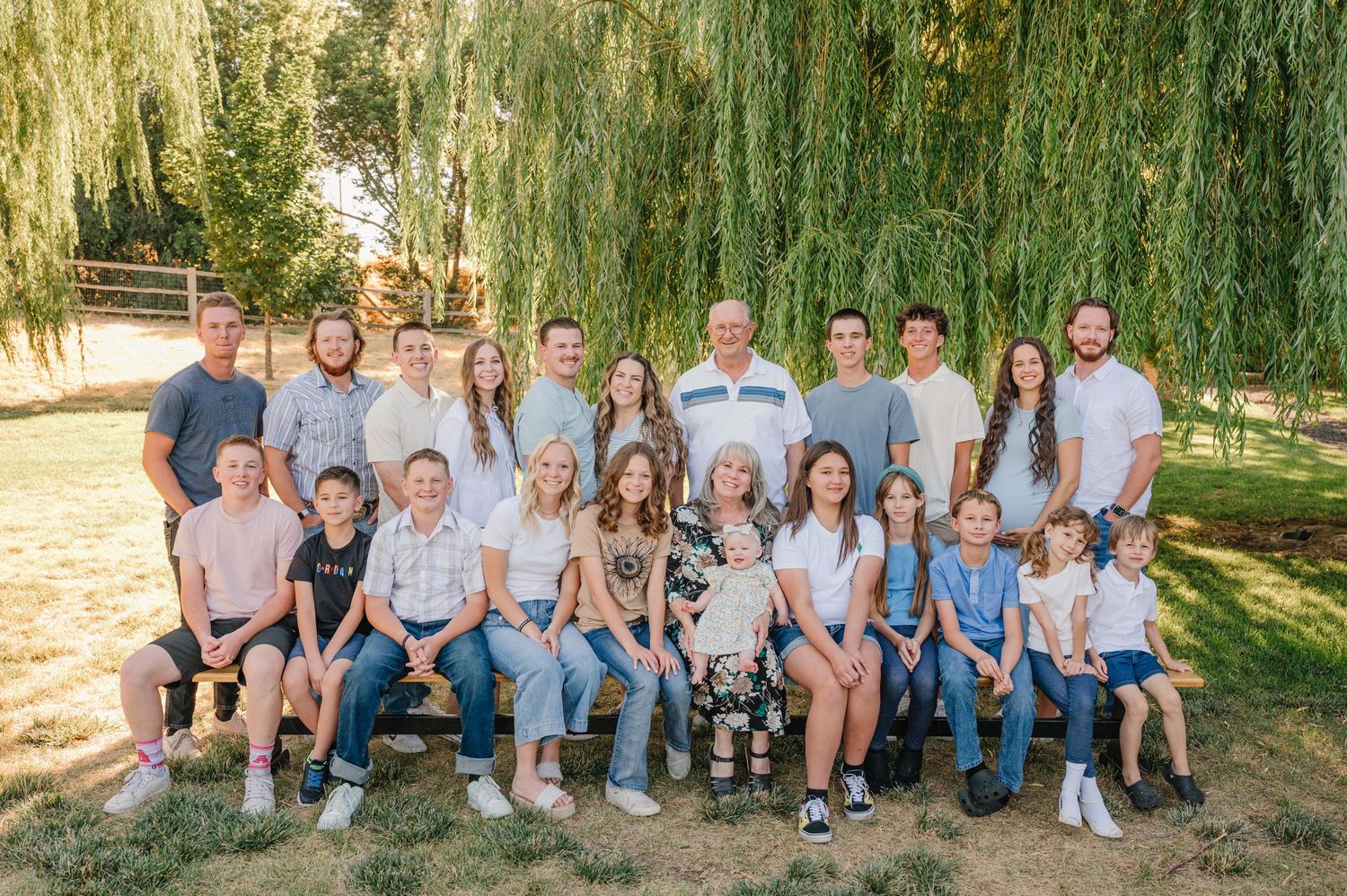 Large family group portrait gathered under a weeping willow tree on a sunny day.
