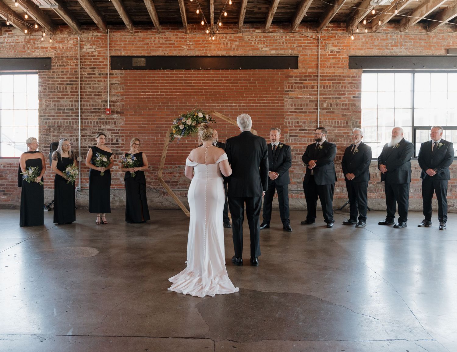 A panoramic view of a wedding ceremony in a rustic brick venue with exposed beams and guests standing in formation.