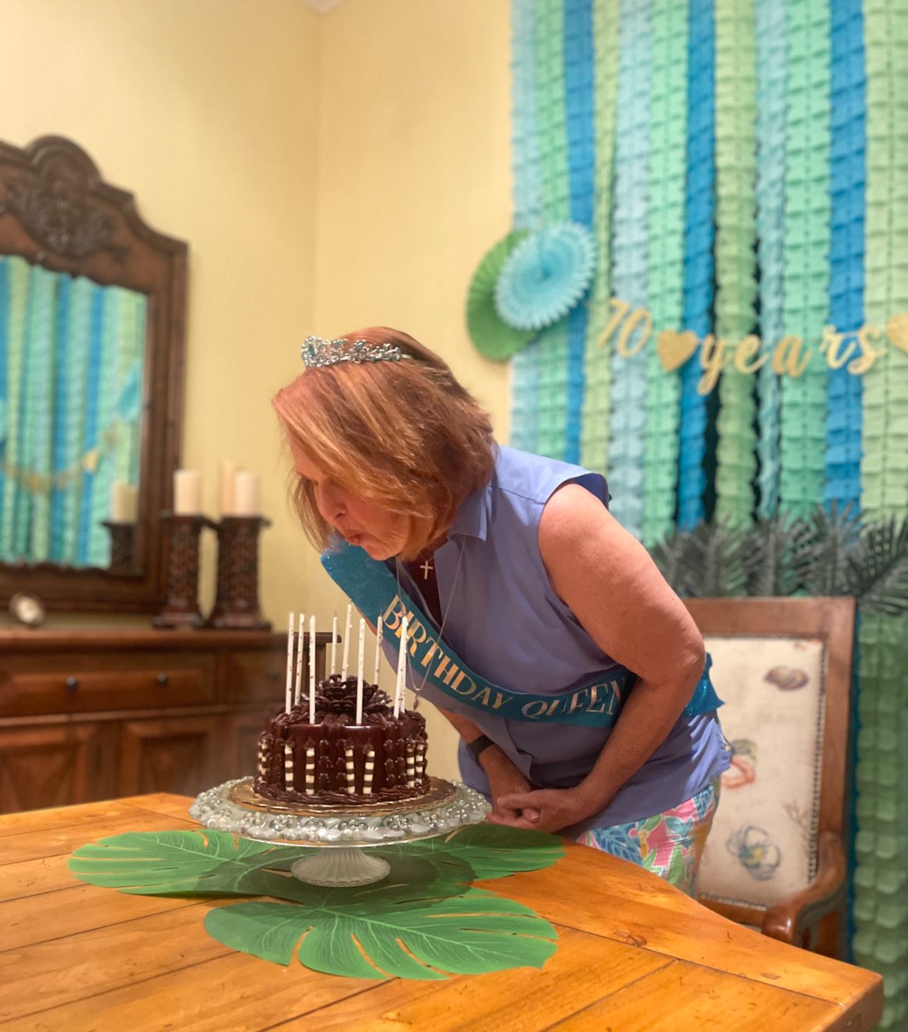 Woman blowing out birthday cake candles with blue and green streamer party decorations.