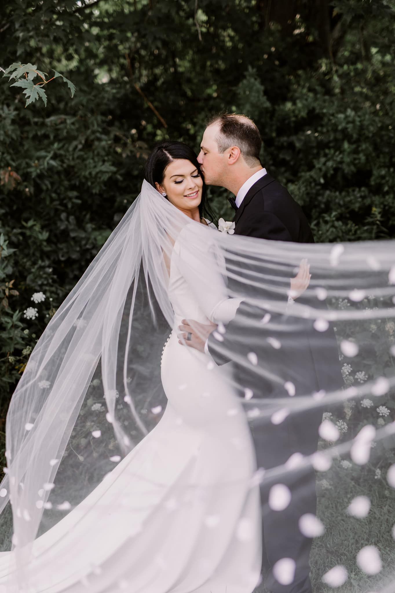 Elegant bridal portrait with flowing veil creating dreamy effect in garden setting.