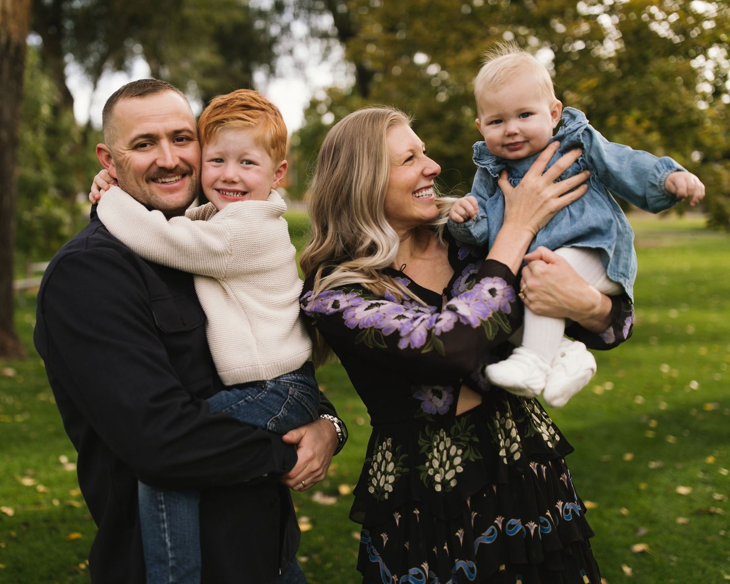 Family of four playing together and laughing in park during autumn.