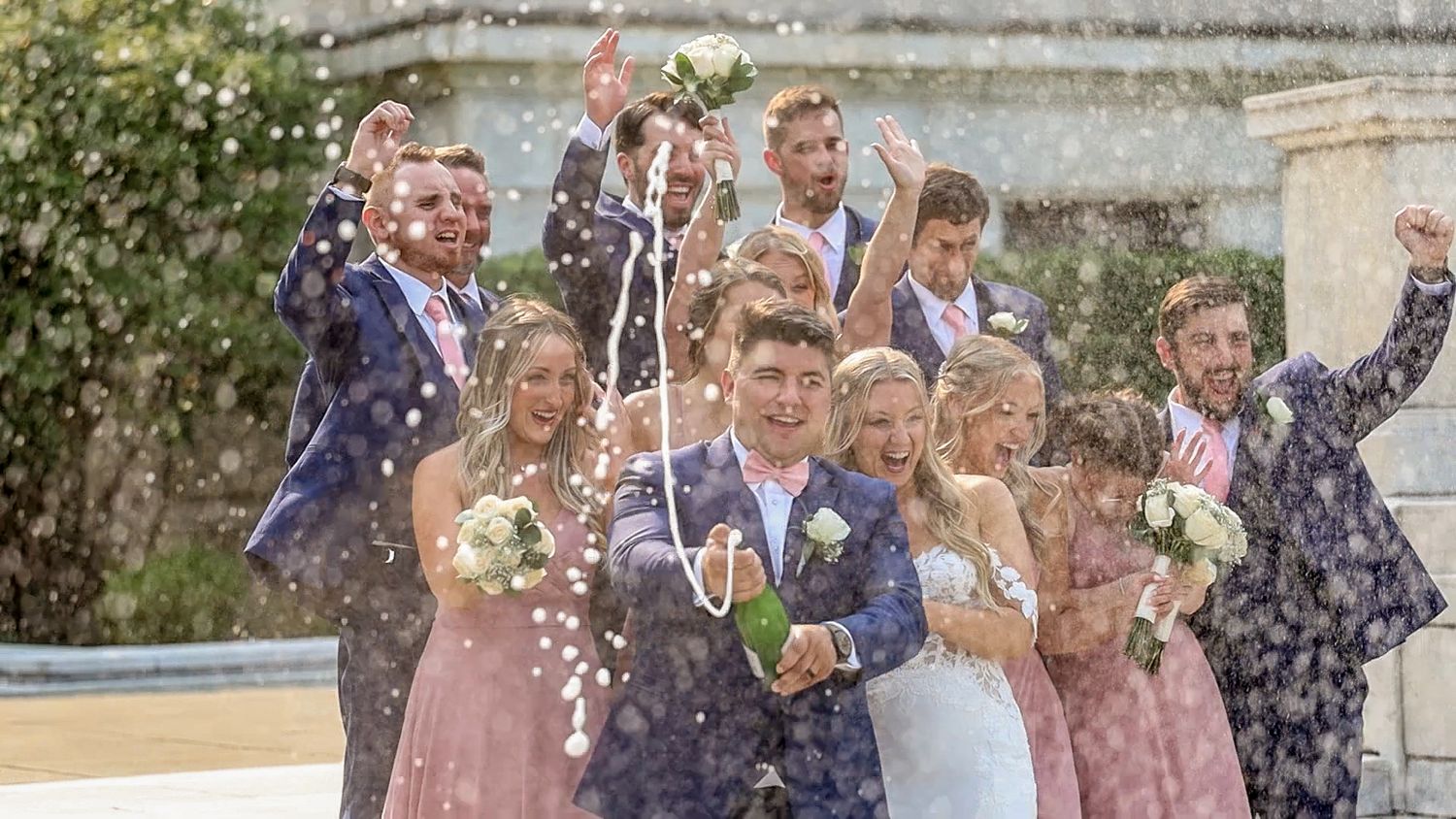 Wedding party celebrates outdoors with confetti being thrown in the air during a joyful summer celebration.