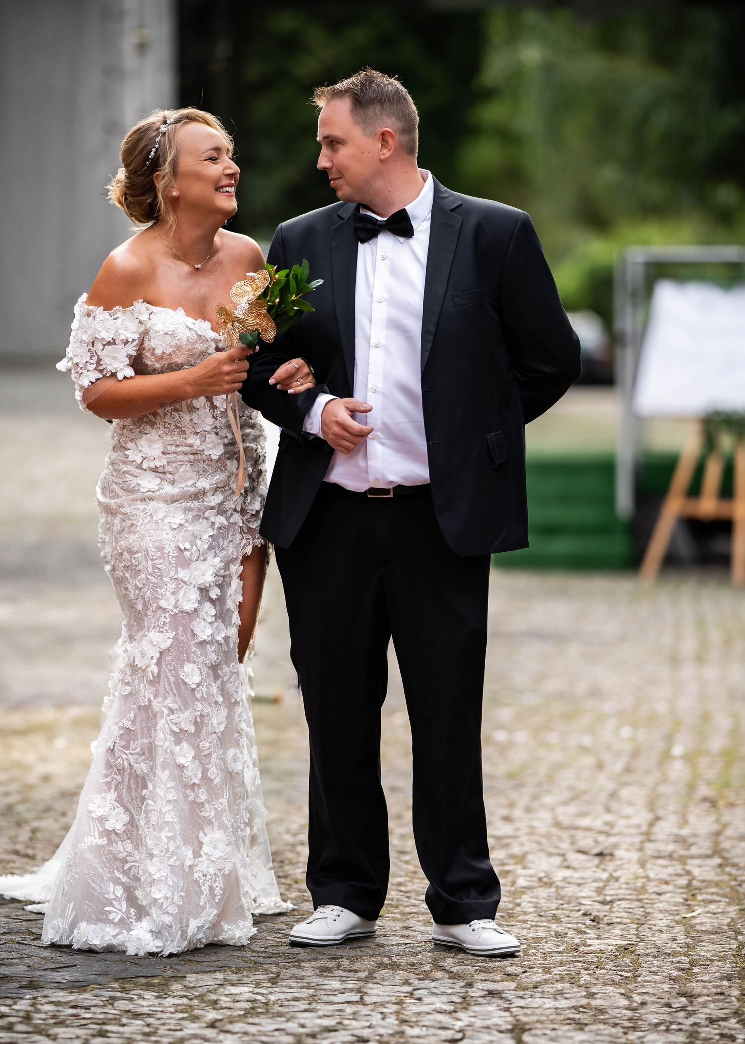 Newlyweds share a joyful moment walking together on cobblestone, bride wearing intricate lace gown and groom in classic tuxedo.