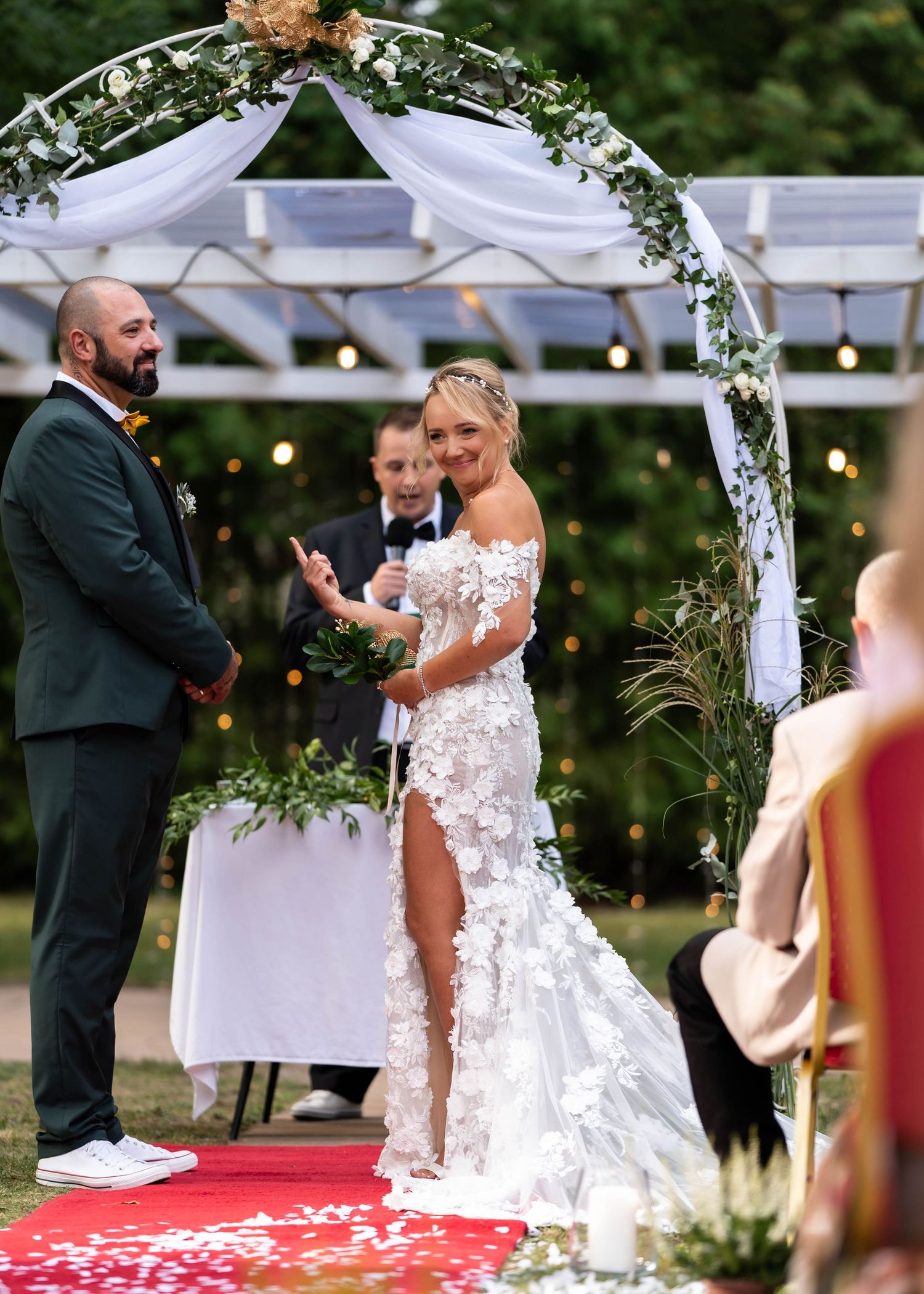 Wedding ceremony under floral arch with bride in white lace dress and groom in dark suit.