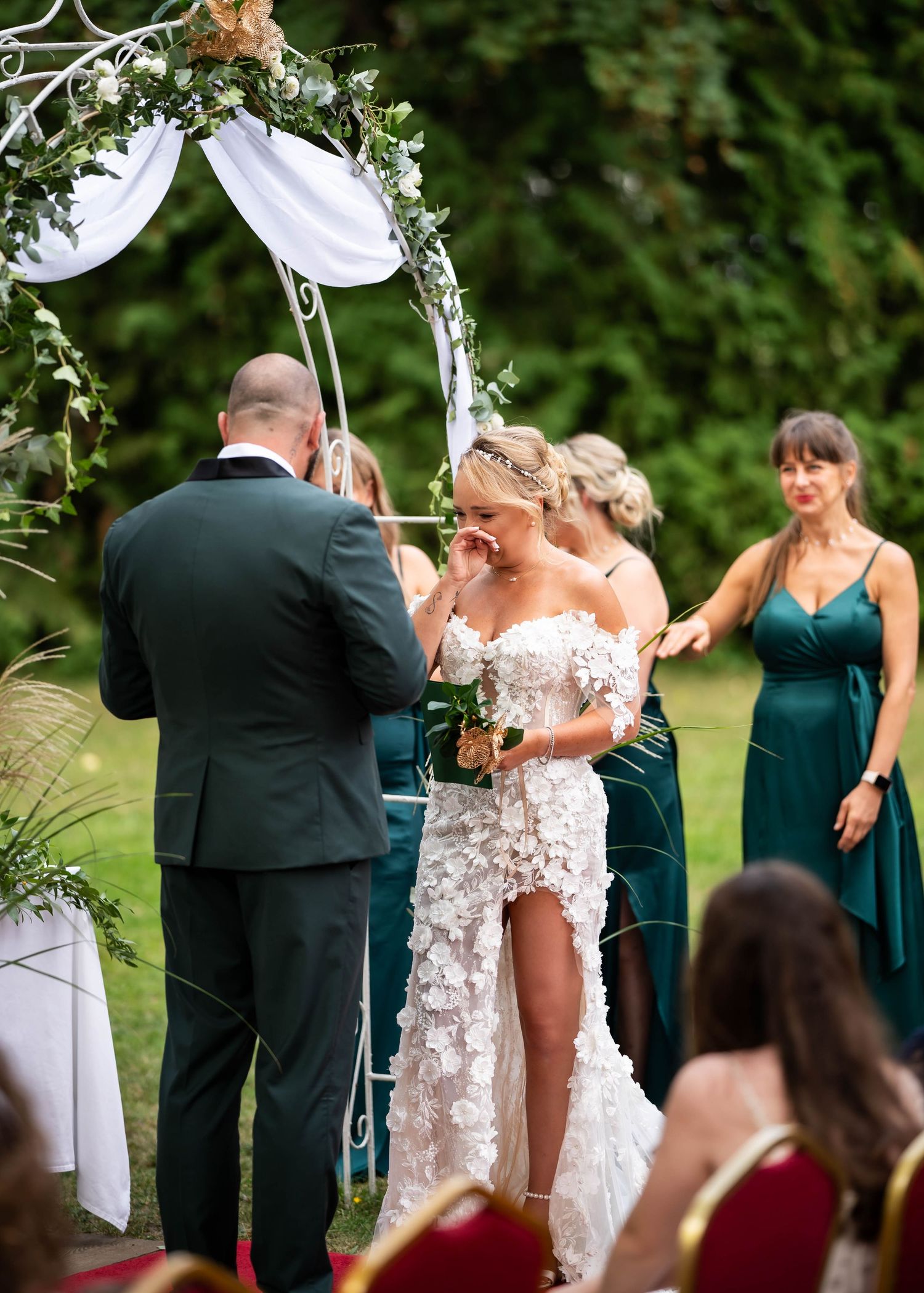 Wedding ceremony under white draped arch with florals as couple exchanges vows.