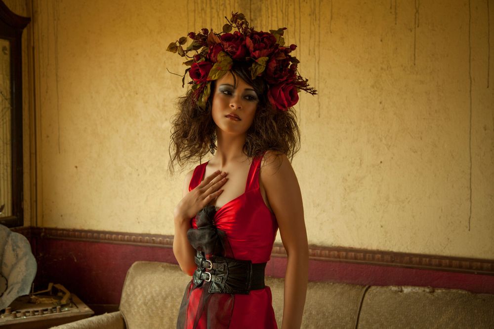 Vintage-inspired portrait with red dress and floral crown in atmospheric indoor setting.
