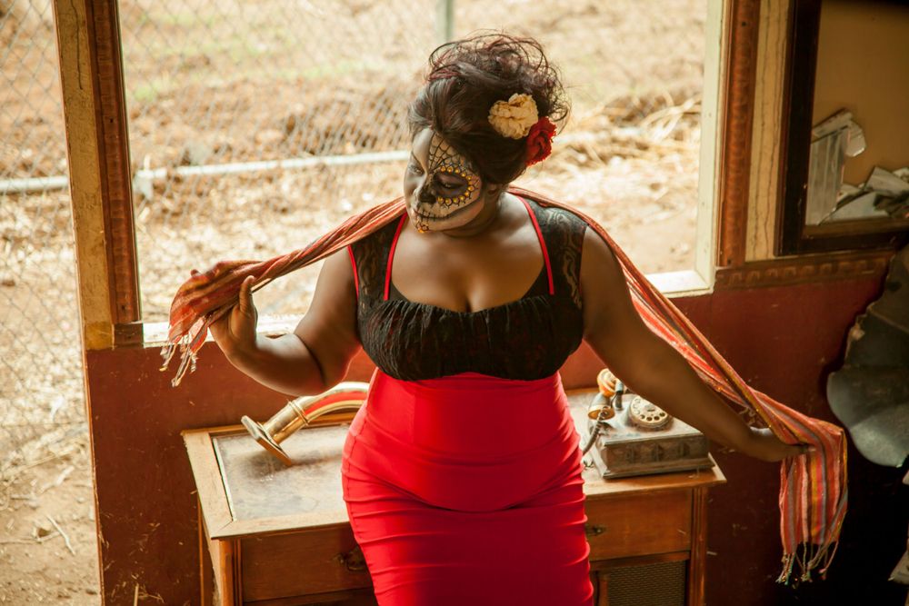 Dramatic pose in a black top and red skirt near a rustic wooden piece of furniture.
