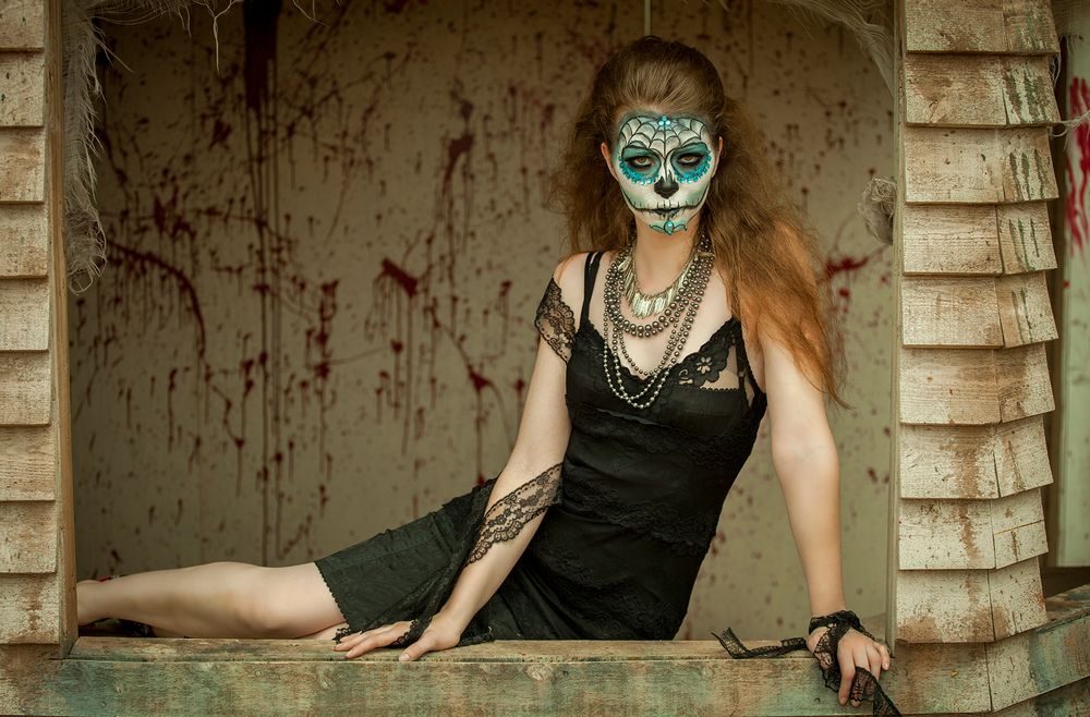 Gothic style portrait with teal face paint and dark dress in spooky setting.