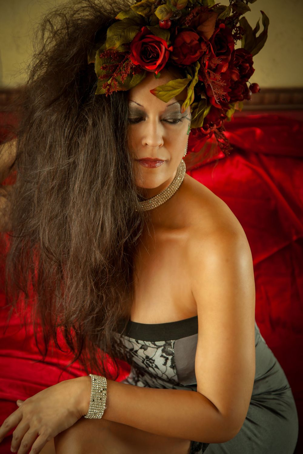 Glamour portrait featuring long dark hair adorned with red roses against a dramatic red backdrop.