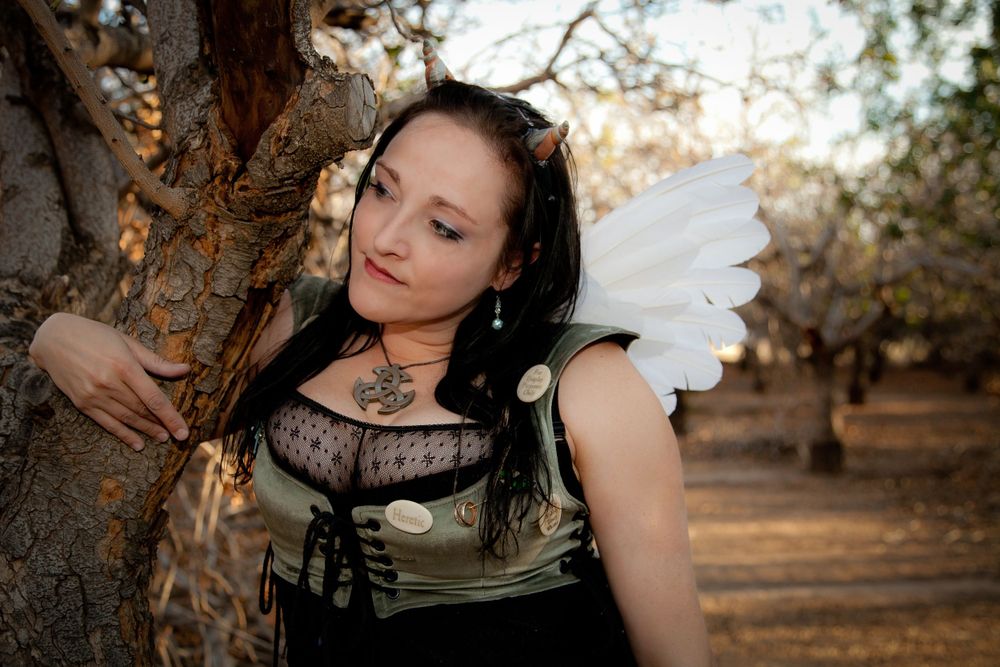 Fantasy themed portrait of figure with white wings leaning against tree trunk.
