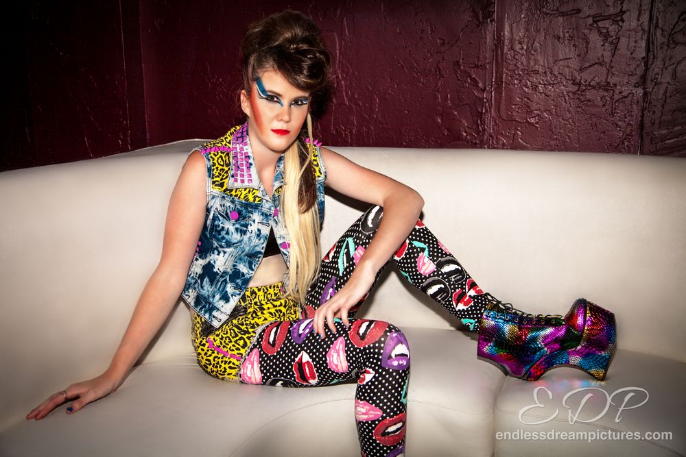 Fashion model poses in vibrant patterned outfit on white couch.