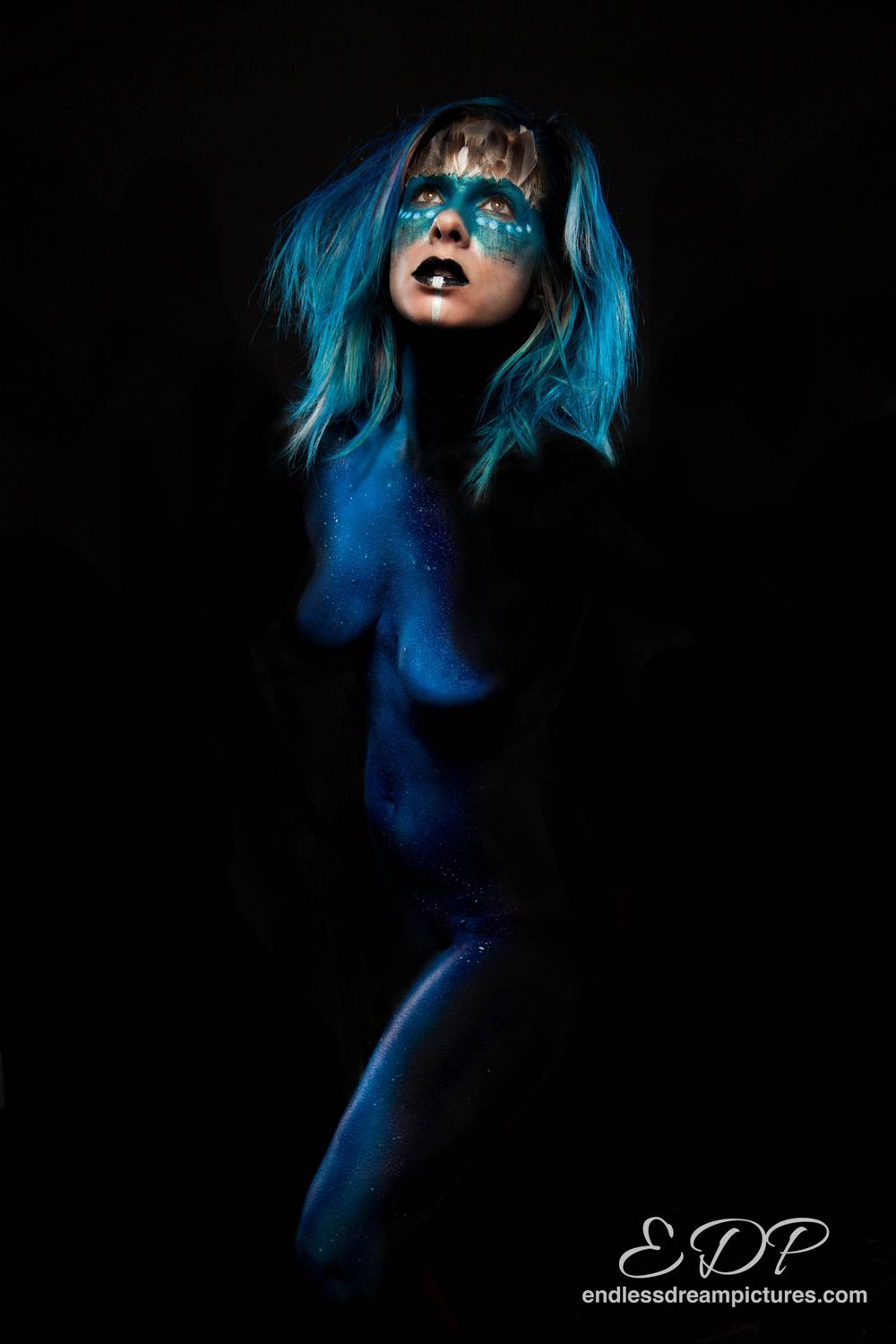Artistic portrait with bright blue hair and makeup against dark background.