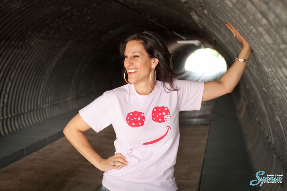 Casual portrait in metal tunnel wearing pink t-shirt with smiley face design.