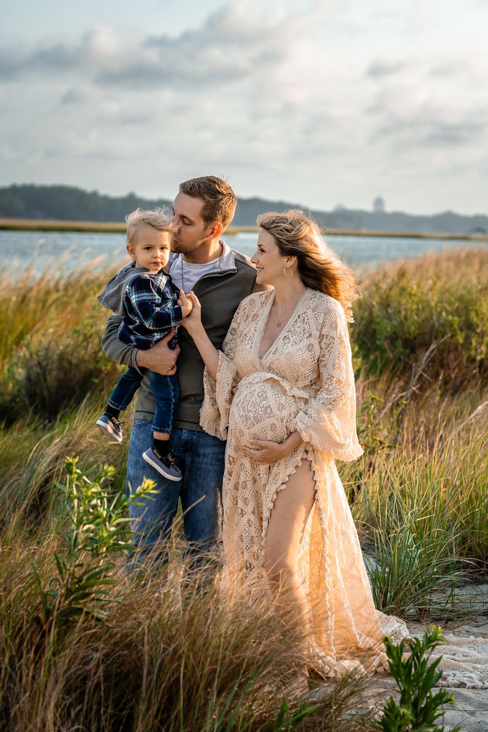 A family maternity photo in coastal marshland during golden hour shows tender family moments.