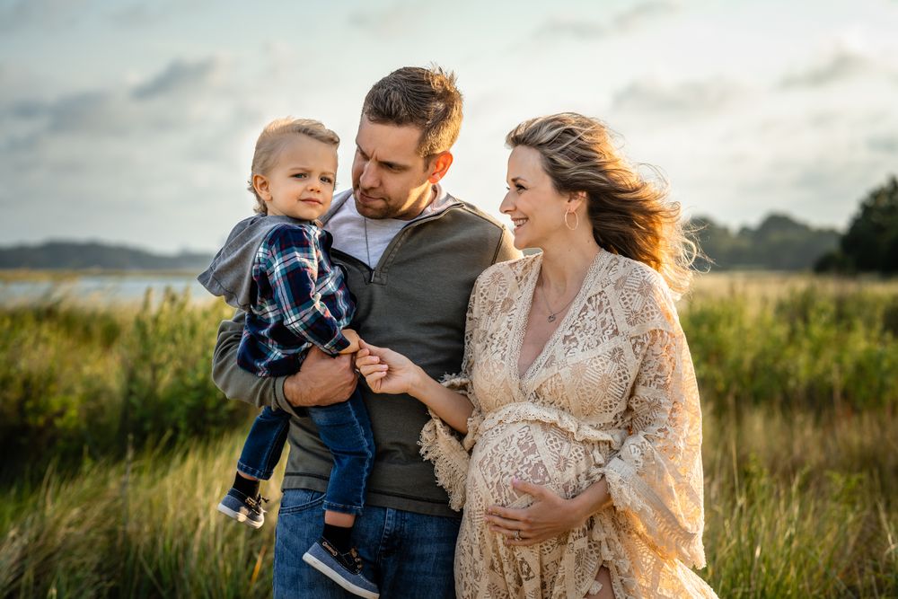 A tender family moment captured at sunset in a grassy field beside water.