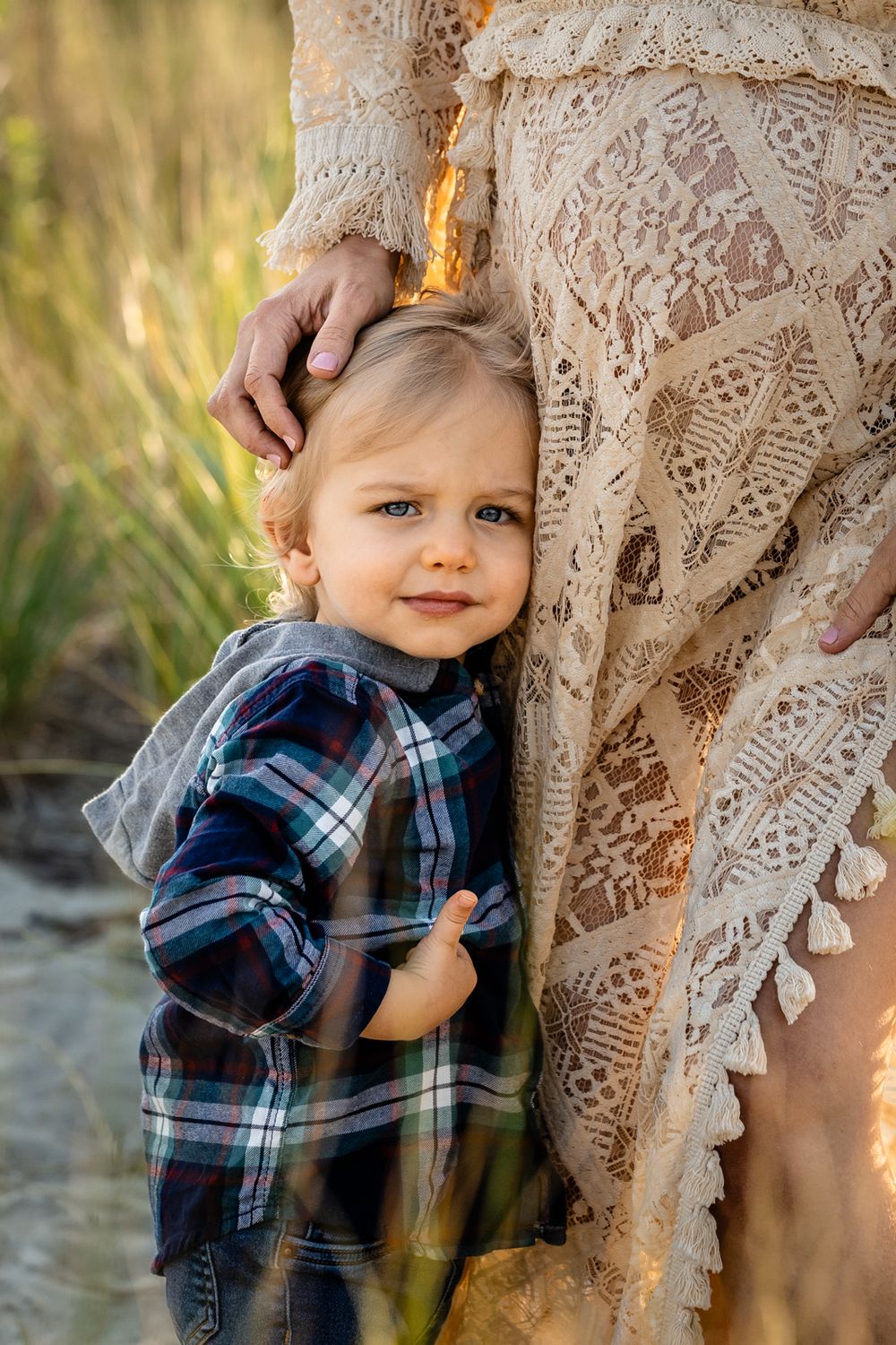 A close-up shot shows a toddler in plaid hugging against a lace dress in warm sunlight.