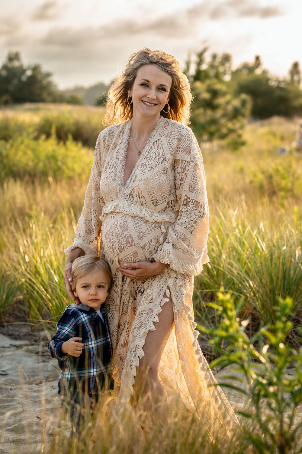 Tender maternity moment captured in natural setting with elegant lace dress at sunset.