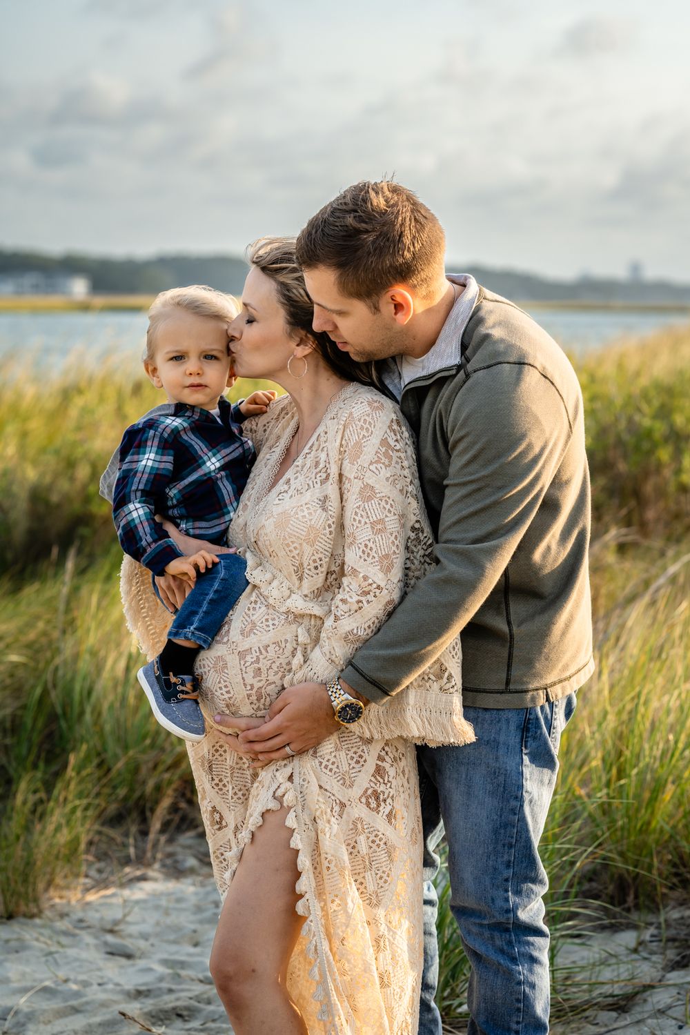 An intimate maternity photo of a family embracing on a sandy beach at sunset.
