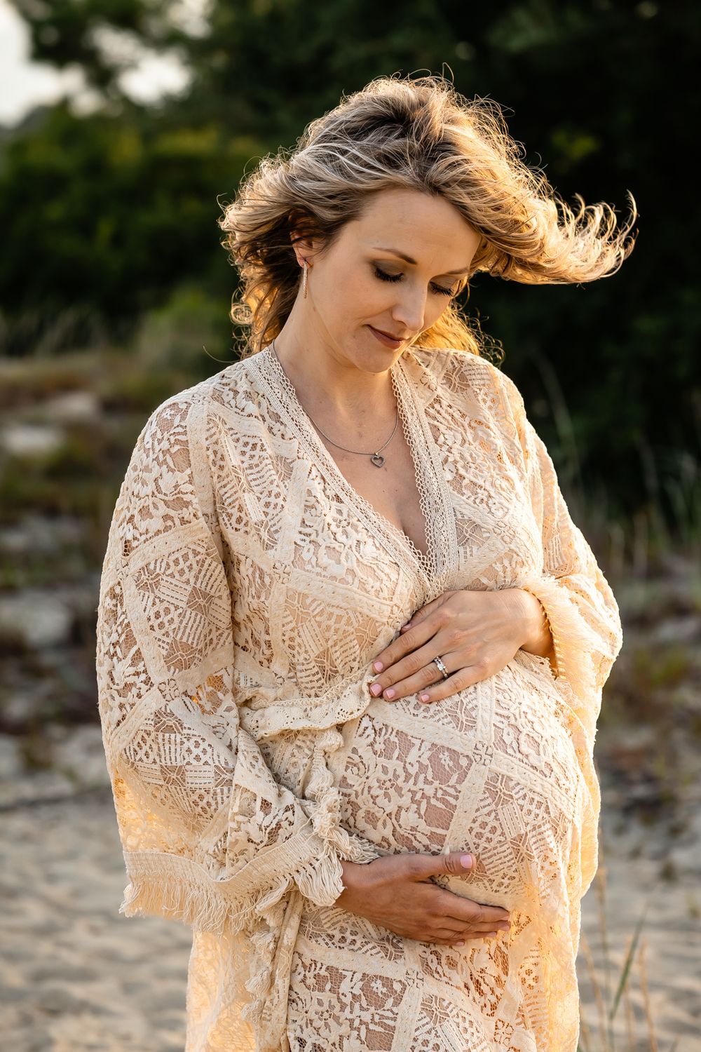 A dreamy maternity portrait featuring a woman in a lace dress with wind-swept hair.