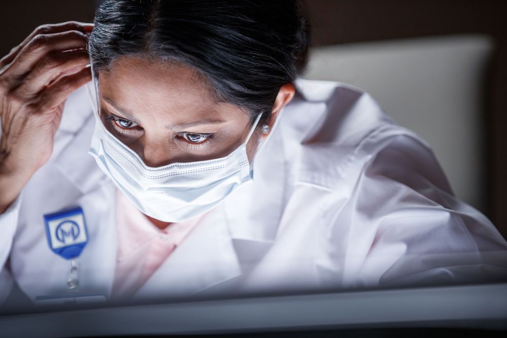 Medical professional in protective mask examining specimen in lab.