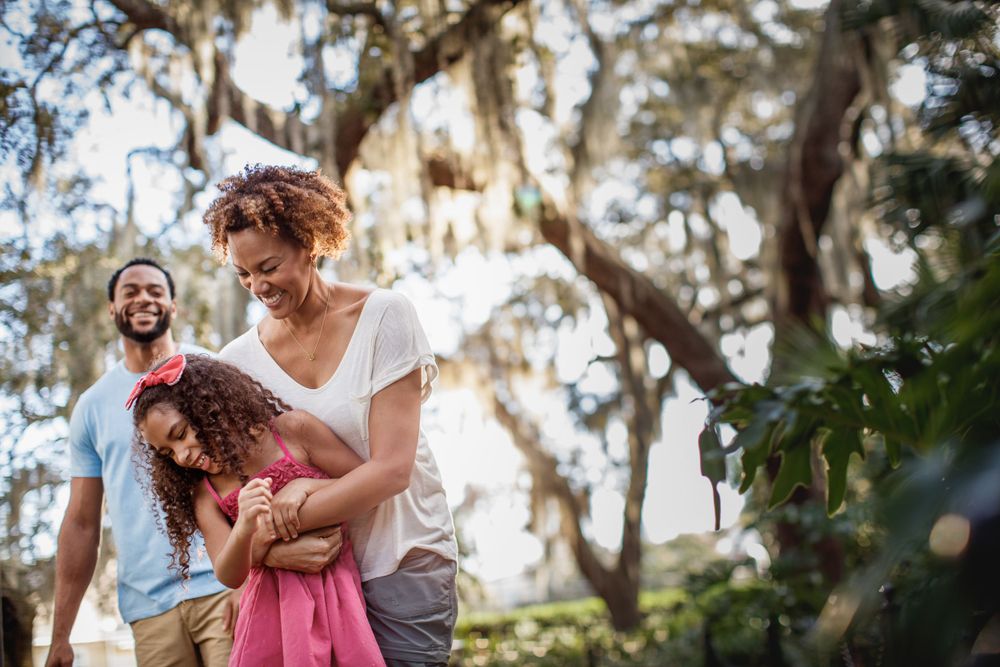Family enjoying playful moment together outdoors under moss-draped trees.