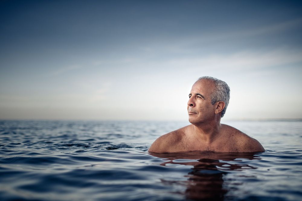 Person swimming in calm blue ocean waters at dusk with scenic horizon view.